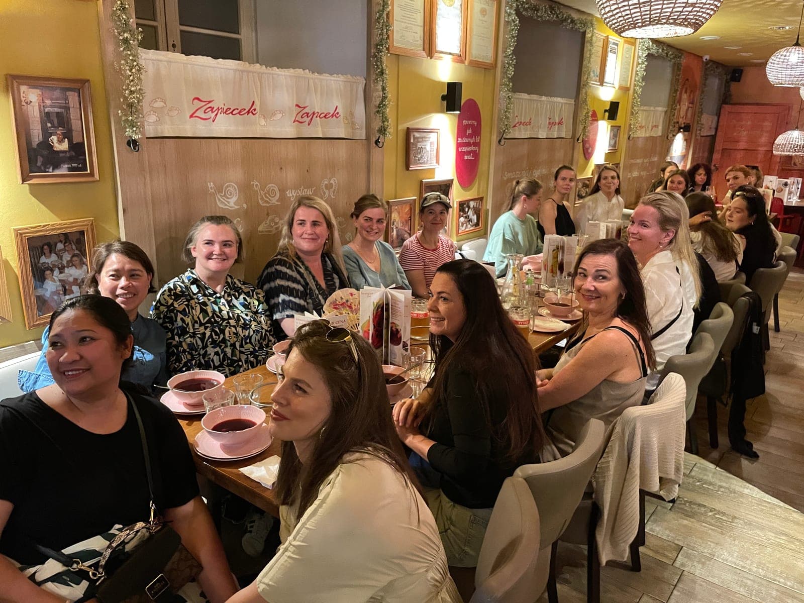 A large private group smiling over pink bowls of barszcz at a long table in a Warsaw pierogi restaurant